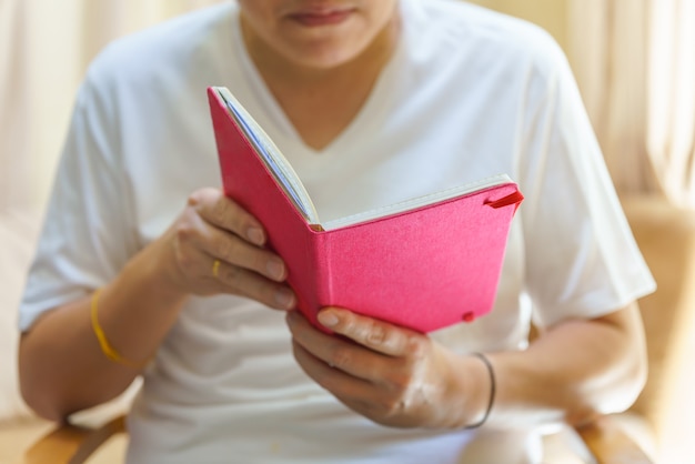 Un uomo che indossa una maglietta bianca seduto e legge un libro.