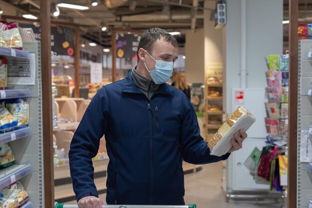 Un uomo che indossa una maschera facciale protettiva sceglie i biscotti al supermercato Cibo e bevande