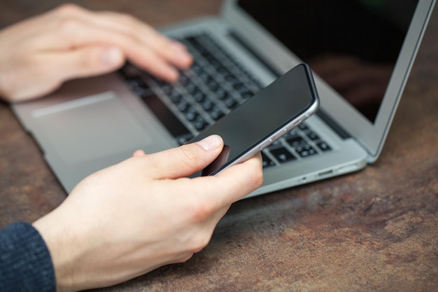 Un uomo che lavora al suo laptop digitando un messaggio sul telefono