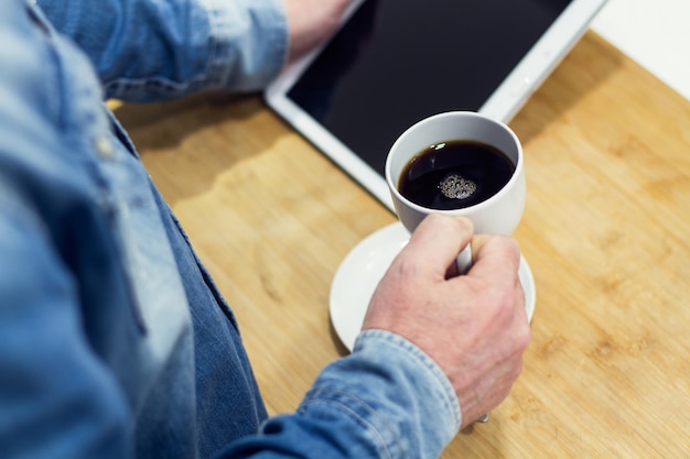 Un uomo che lavora con un tablet e con una tazza di caffè in mano