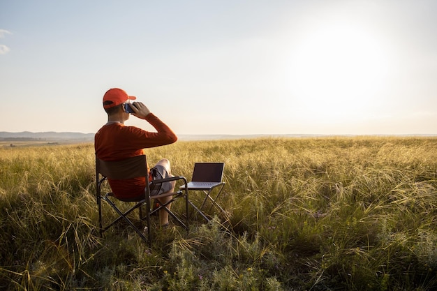 Un uomo che lavora su un laptop si rilassa in un campo all'alba Concetto di lavoro remoto