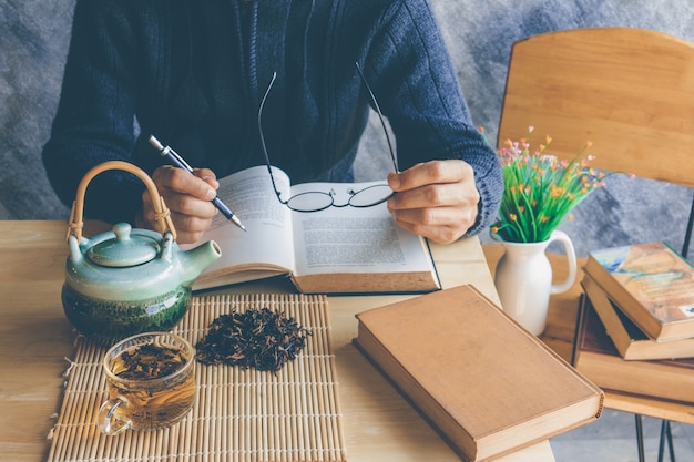 Un uomo che legge il libro con una tazza di tè e vecchio libro sul tavolo