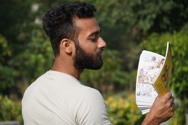 Un uomo che legge un libro con sfondo sfocato di vegetazione