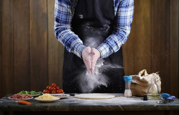 Un uomo che prepara una pizza, impasta l'impasto e mette gli ingredienti