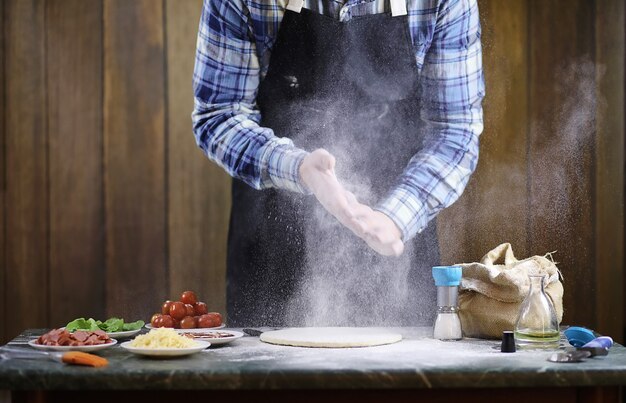 Un uomo che prepara una pizza, impasta l'impasto e mette gli ingredienti