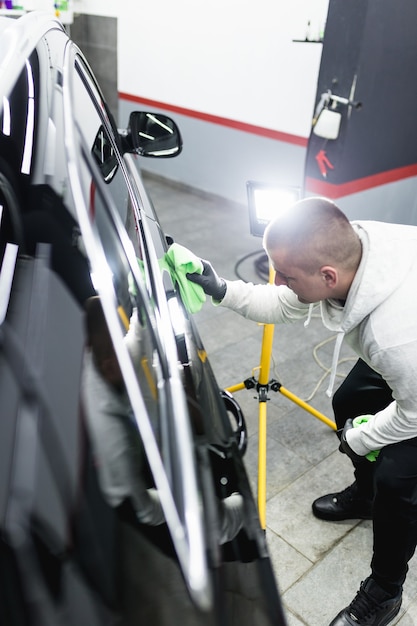 Un uomo che pulisce l'auto con un panno in microfibra, il concetto di dettagli dell'auto (o valeting). Messa a fuoco selettiva.