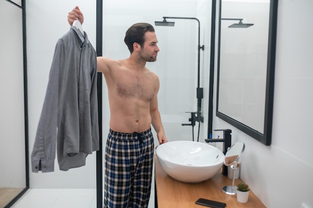 Un uomo che sceglie i vestiti e tiene in mano una camicia grigia