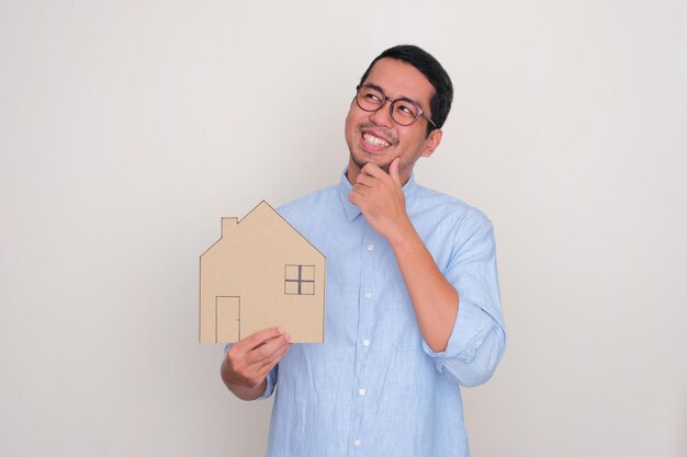 Un uomo che sorride e guarda a destra mentre tiene in mano un cartone a forma di casa