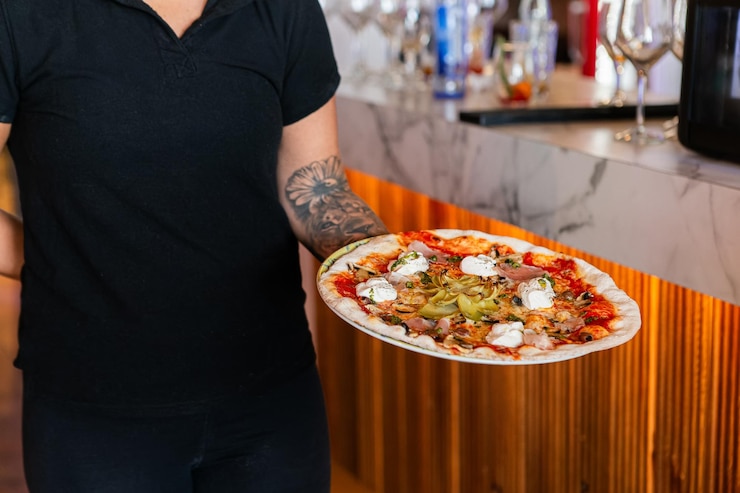 Foto un uomo che tiene una pizza con un tatuaggio sul braccio