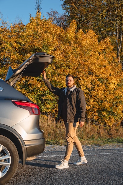 Un uomo chiude il bagagliaio della sua auto dietro la foresta autunnale