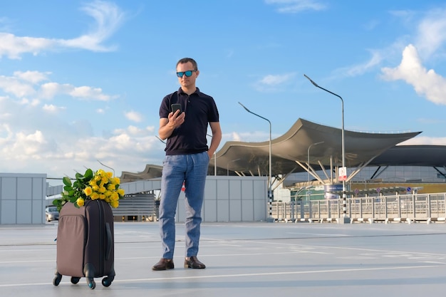 Un uomo con bagagli e un bouquet di rose gialle mentre aspetta un volo in un parcheggio dell'aeroporto