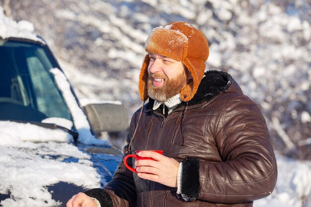 un uomo con barba e baffi che indossa un cappello di pelliccia e una giacca in una giornata di sole in una foresta invernale