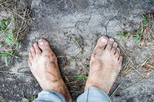 Un uomo con i piedi sporchi sta in piedi a terra screpolato dal caldo