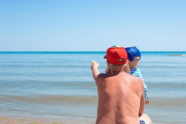 Un uomo con il nipote in riva al mare mostra la mano al mare Buon fine settimana estivo