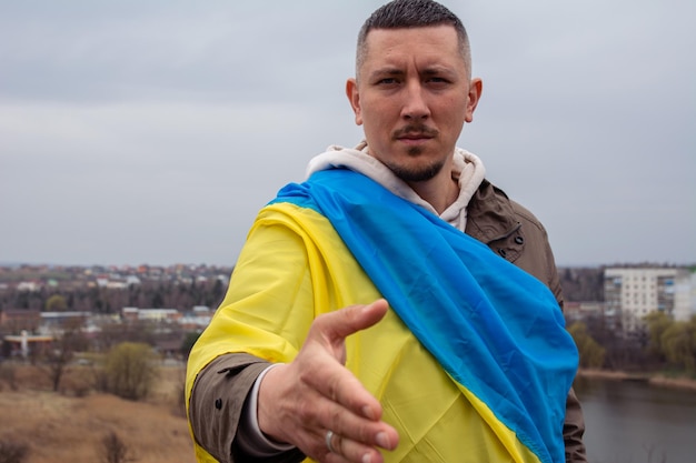 Un uomo con la bandiera dell'Ucraina tende la mano per una stretta di mano contro la città ucraina