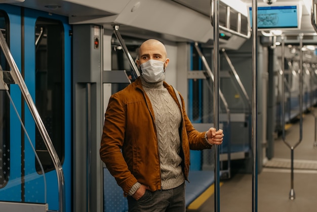 Un uomo con la barba e una maschera medica per evitare la diffusione di COVID-19 sta guidando un vagone della metropolitana e tiene il corrimano. Un ragazzo calvo con una mascherina chirurgica sta mantenendo le distanze sociali su un treno.