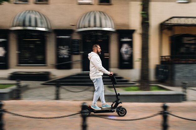 Un uomo con la barba in abiti bianchi gira velocemente per la città su uno scooter elettrico.