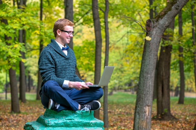 Un uomo con lap top su un piedistallo che finge di essere una statua nel parco in autunno. Fatti un'idea