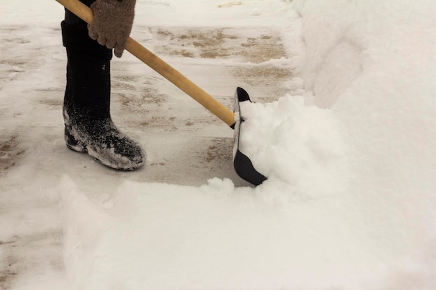 Un uomo con stivali di feltro, con una pala in mano, rimuove la neve dal marciapiede dopo una nevicata.