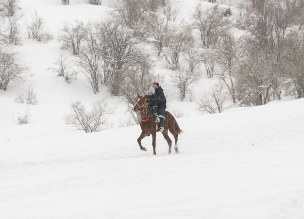 Un uomo con un bambino a cavallo in montagna d'inverno