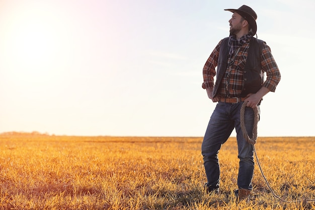 Un uomo con un cappello da cowboy e un loso nel campo. Contadino americano in un campo che indossa un cappello di jeans e con un loso. Un uomo sta attraversando il campo con un cappello