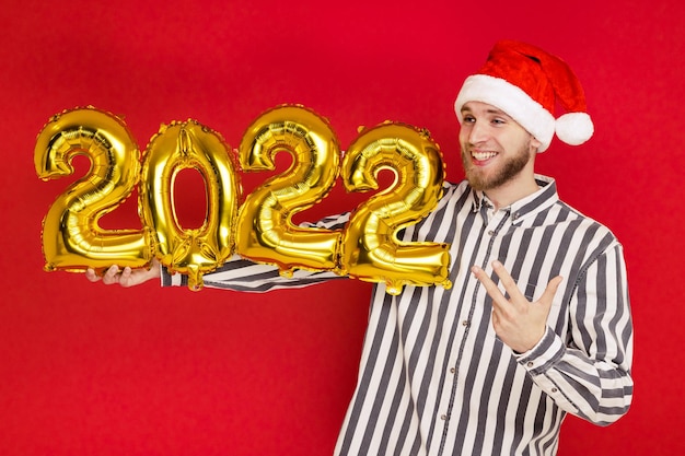 Un uomo con un cappello di Natale tiene in mano i numeri 2022. Il nuovo anno sta arrivando