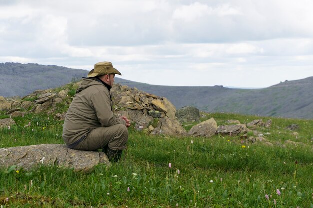 un uomo con un cappello e abiti da viaggio siede su una pietra in un paesaggio montano deserto