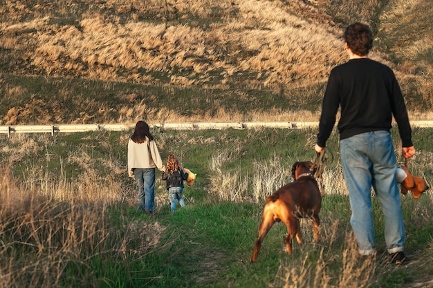 un uomo con un grosso cane al guinzaglio guarda sua moglie e sua figlia