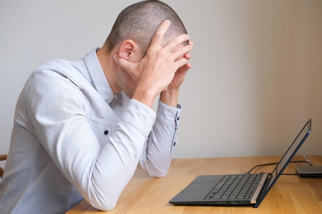 Un uomo con un laptop è stressato e si tiene la testa per il mal di testa