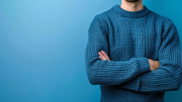 Un uomo con un maglione blu con le braccia incrociate sta in piedi su uno sfondo blu