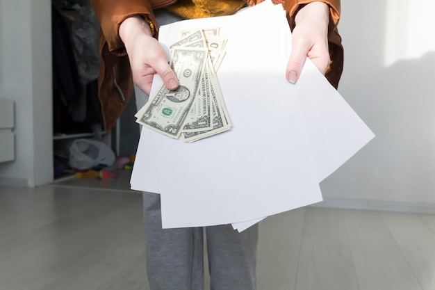 Un uomo con un maglione giallo e una giacca con documenti in mano e denaro Il concetto di crisi economica e grandi bollette nelle case