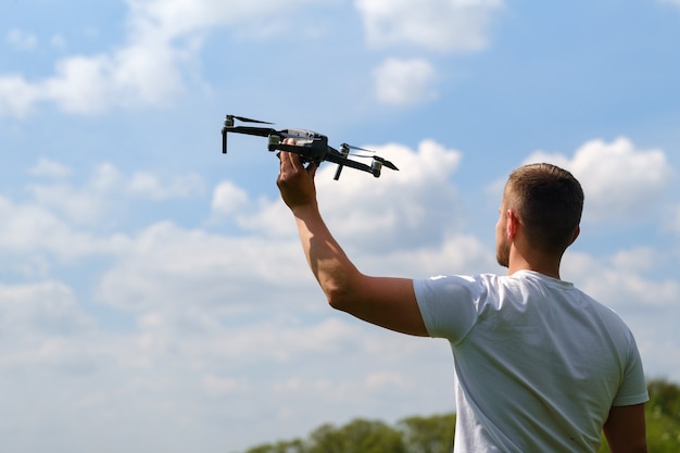 Un uomo con un quadricottero in mano, alzato al cielo in natura.