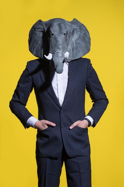 Un uomo con un vestito e una maschera di elefante su sfondo giallo. Sfondo concettuale di affari