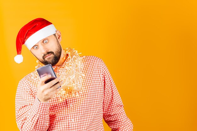 Un uomo con una camicia a quadri di Capodanno, che tiene un telefono davanti a sé e guarda sorpreso