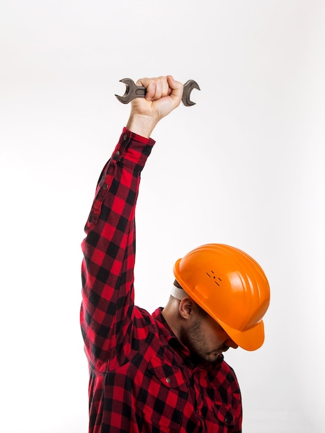 Un uomo con una camicia a quadri e un casco da costruzione con una chiave in mano isolata