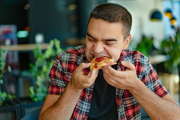 Un uomo con una camicia a quadri mangia una deliziosa pizza con formaggio, salsiccia e salsa nel ristorante.