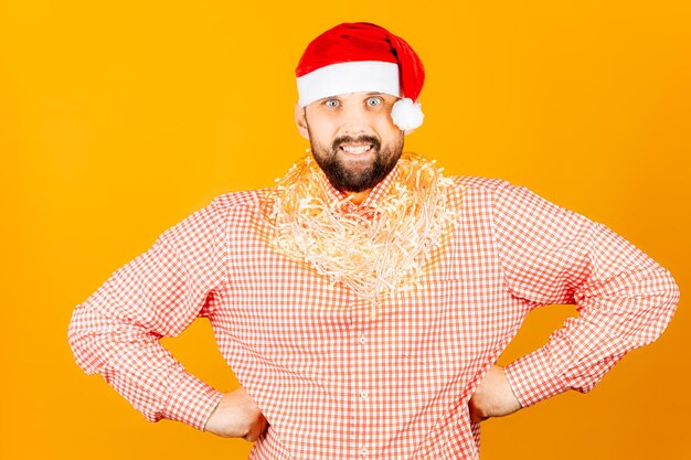 Un uomo con una camicia a quadri rosa su uno sfondo giallo che indossa un cappello di Babbo Natale e una ghirlanda intorno al collo