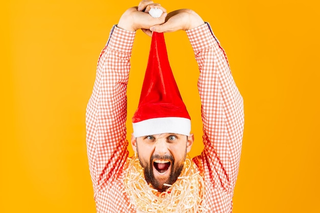 Un uomo con una camicia a quadri rossa su uno sfondo giallo tira su i berretti di Babbo Natale di Capodanno