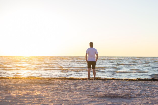 Un uomo con una camicia bianca e pantaloncini marroni in piedi sulla spiaggia vuota all'alba