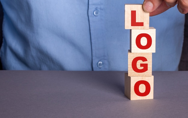 Un uomo con una camicia blu compone verticalmente la parola LOGO da cubi di legno