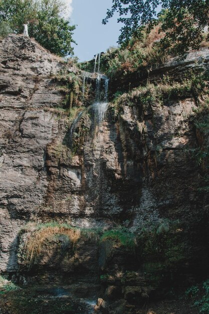 Un uomo con una camicia rossa è in piedi davanti a una cascata