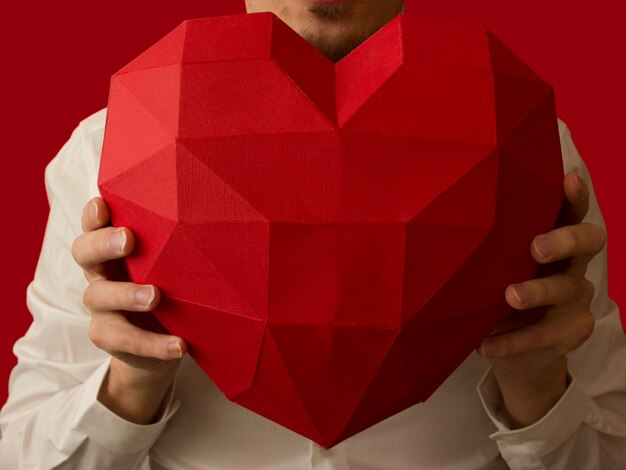 Un uomo con una camicia tiene un grande cuore insolito nelle sue mani. concetto di San Valentino.