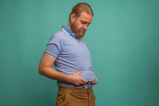 Un uomo con una faccia triste sente la sua pancia grassa su sfondo blu primo piano Spazio per il testo