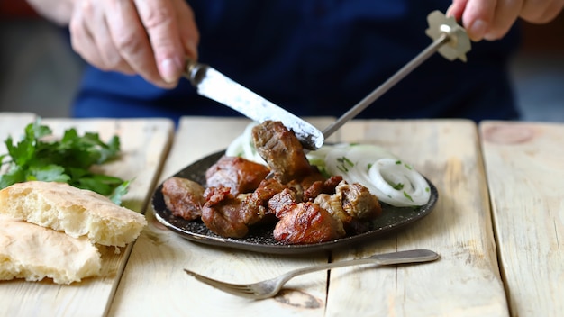 Un uomo con una forchetta e un coltello mangia un barbecue con cipolle. Un piatto con un kebab.