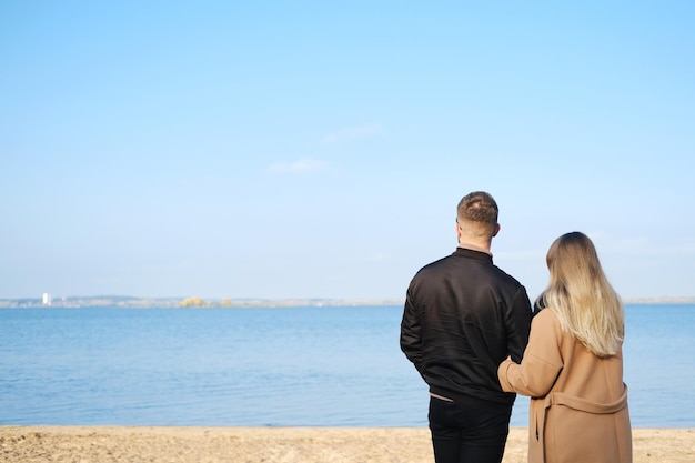 Un uomo con una giacca nera e una donna con un caldo cappotto marrone stanno con le spalle alla telecamera e guardano il lago