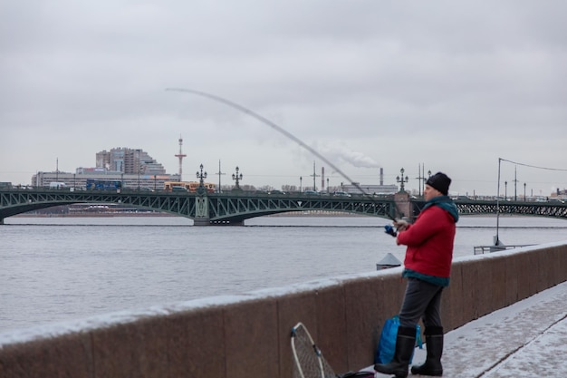 Un uomo con una giacca rossa sta pescando in acqua con un ponte sullo sfondo.