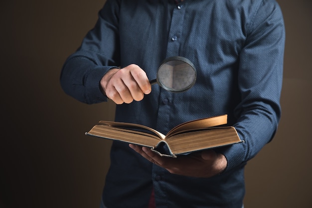 Un uomo con una lente d'ingrandimento legge un libro su una superficie marrone