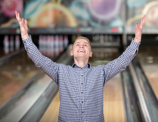 Un uomo con una maglietta alza le mani in un club di bowling.