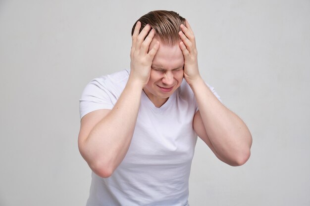 Un uomo con una maglietta bianca si massaggia la testa con le mani. Il concetto di stress profondo da problemi nella vita.