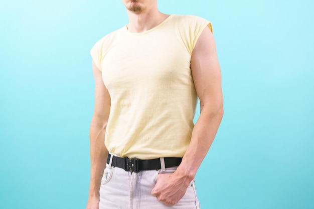 Un uomo con una maglietta gialla senza maniche mise la mano in una tasca su sfondo blu Jeans Elegante modello umano Una persona in posa Camicia che indossa abiti caucasici Sezione centrale Pantaloni moderni